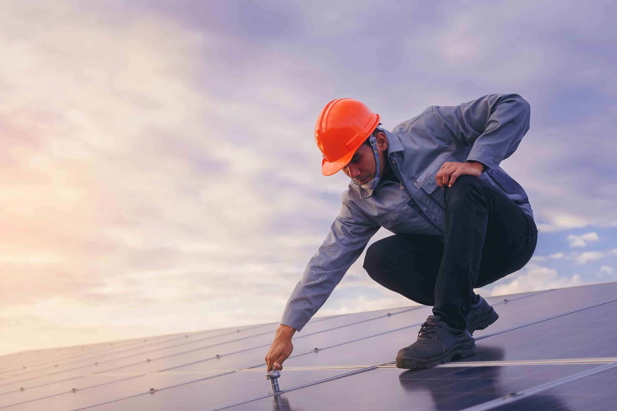 Arbeiter mit Helm montiert oder prüft Solarpanel auf Dach bei Sonnenuntergang.