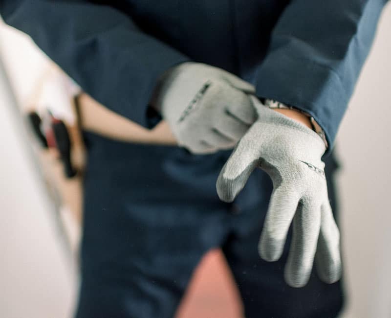 Arbeitshandschuhe anziehen in blauer Arbeitskleidung - E & IT Elektroanlagen GmbH Person zieht graue Arbeitshandschuhe an und trägt blaue Arbeitskleidung mit Werkzeugen im Hintergrund.